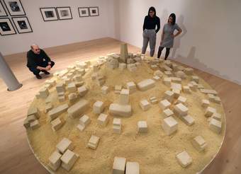 A photograph of three visitors looking at an installation positioned on a low plinth.
