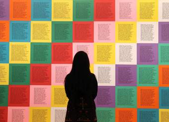 A photograph of a visitor looking at a colourful artwork by Jenny Holzer