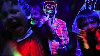Children smiling and shouting in a dark space against a backdrop of neon-painted figures.